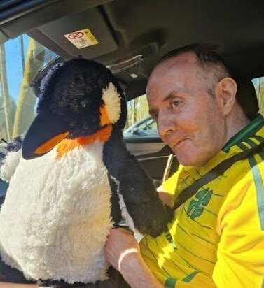 care home resident in a car with a stuffed penguin toy